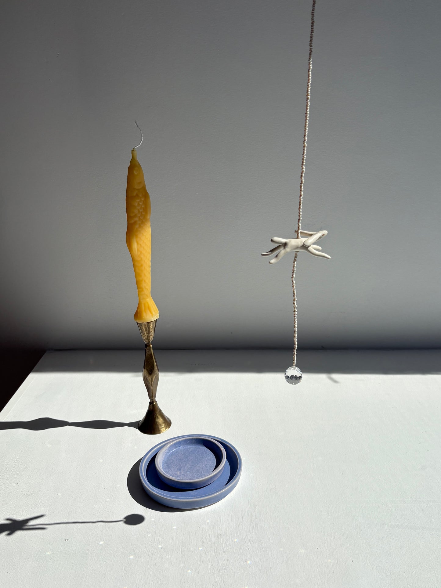Candle, small blue ceramic dish, and hanging starfish on a white surface with gray background